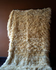 Marie Olsson Nylander Amber Rug hand-woven high-pile longhair wool Fuzzy Shepherd rug in cream beige hanging on a rail.