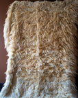 Marie Olsson Nylander Amber Rug hand-woven high-pile longhair wool Fuzzy Shepherd rug in cream beige hanging on a rail.