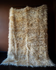 Marie Olsson Nylander Amber Rug hand-woven high-pile longhair wool Fuzzy Shepherd rug in cream beige hanging on a rail.