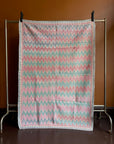 Semi-antique Jaipur Kantha quilt with a pink and mint green chevron zig-zag pattern hanging on a clothing rack against a terracotta wall.