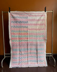 Semi-antique Jaipur Kantha quilt with a two-tone indigo blue and red chevron zig-zag pattern hanging on a clothing rack against a terracotta wall.