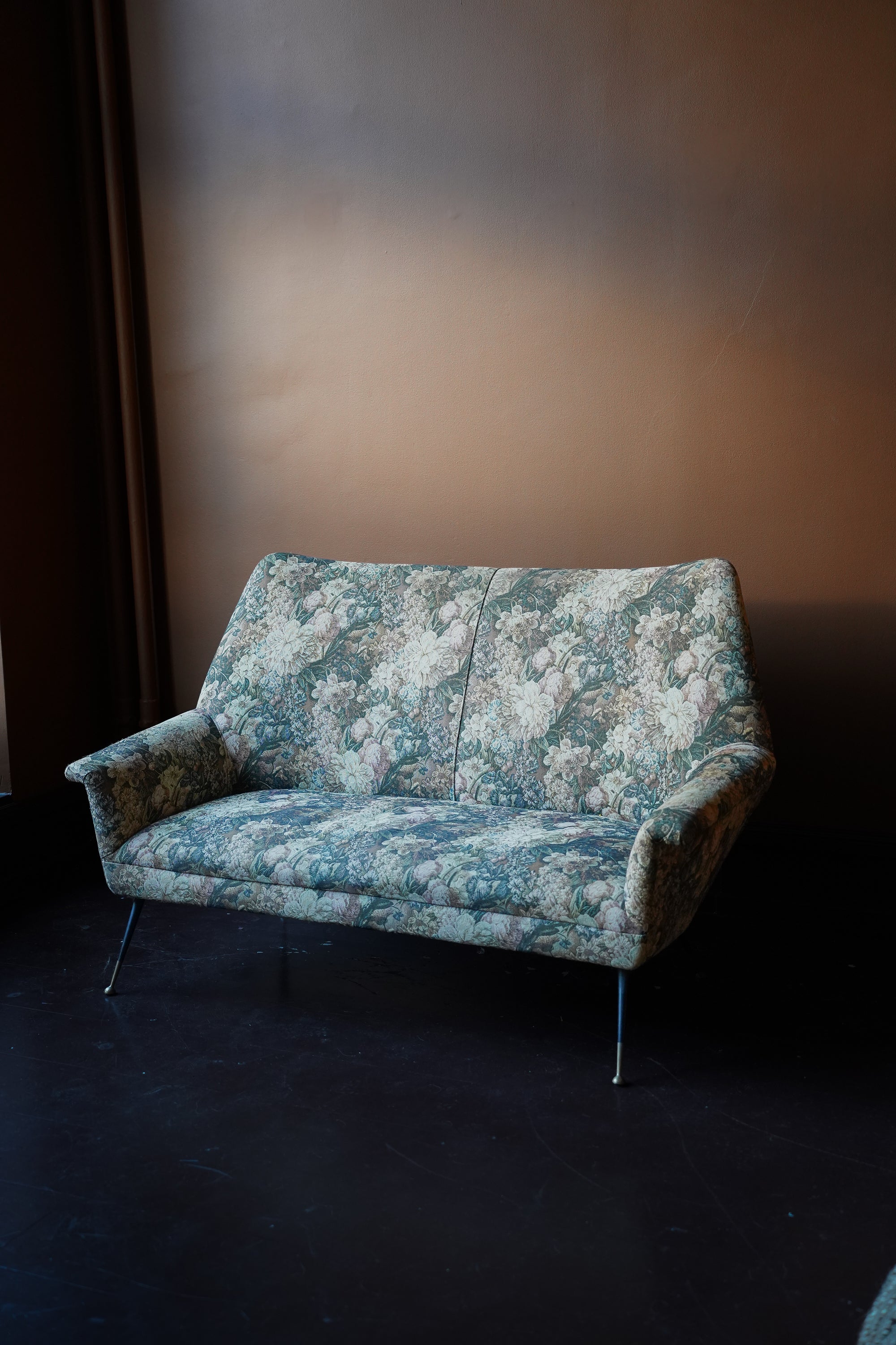 Vintage mid-century modern 2-seater sofa with curved backrest and original floral tapestry upholstery on tapered metal legs with brass feet.
