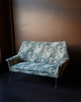 Vintage mid-century modern 2-seater sofa with curved backrest and original floral tapestry upholstery on tapered metal legs with brass feet.
