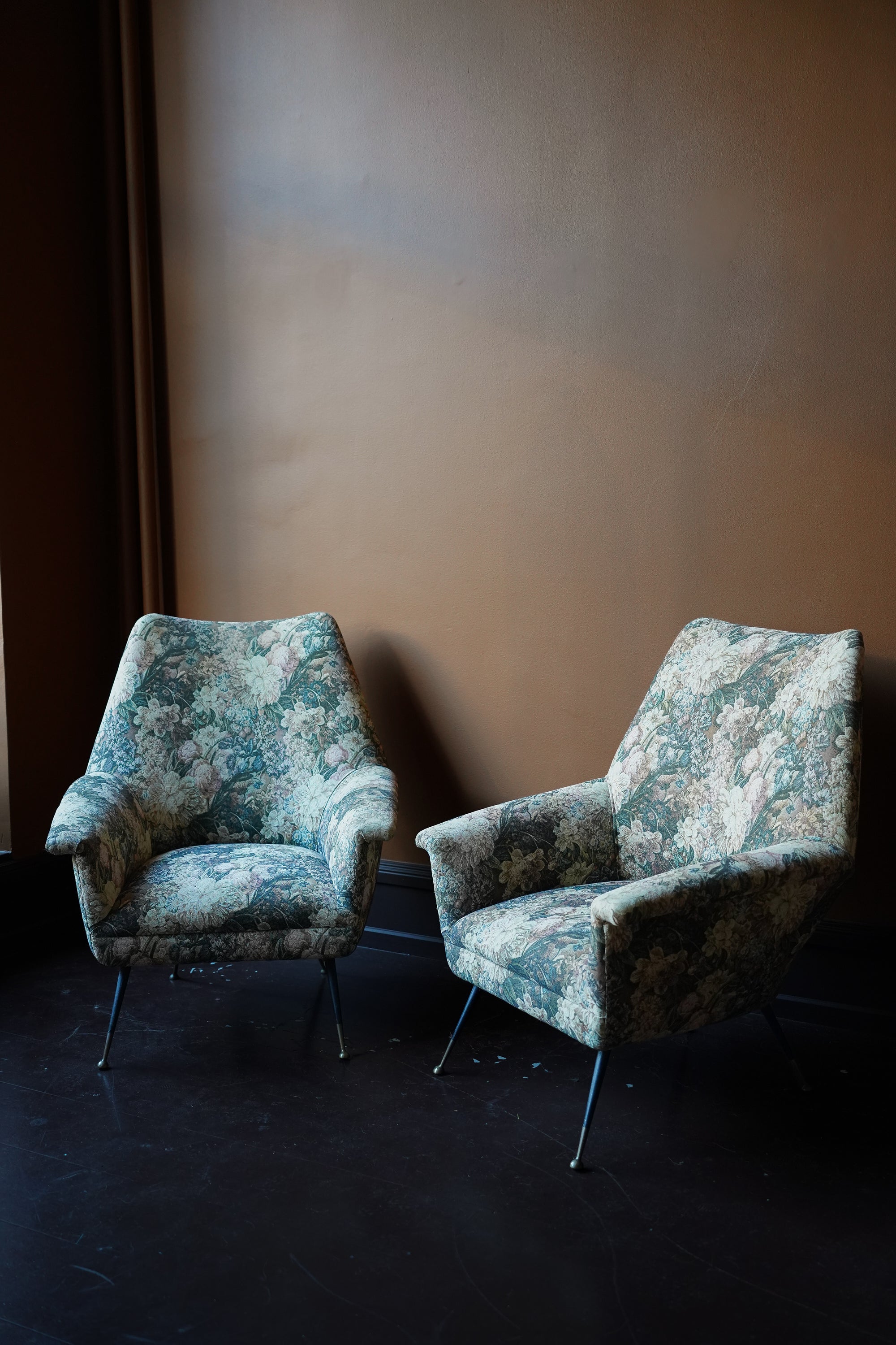 Pair of vintage Italian mid-century modern armchairs with curved backrests and floral tapestry upholstery on tapered metal legs with brass feet.