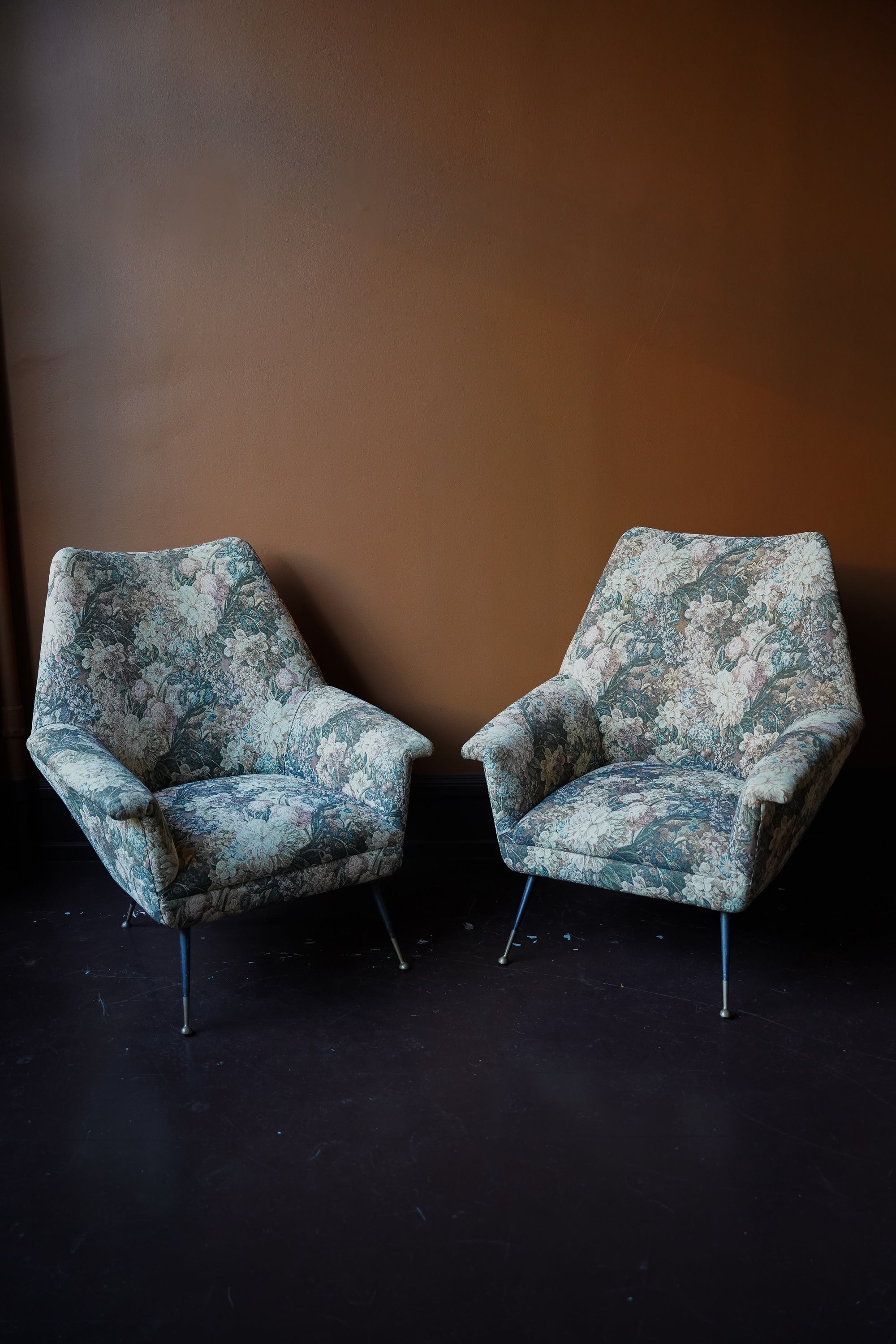 Pair of vintage Italian mid-century modern armchairs with curved backrests and floral tapestry upholstery on tapered metal legs with brass feet.