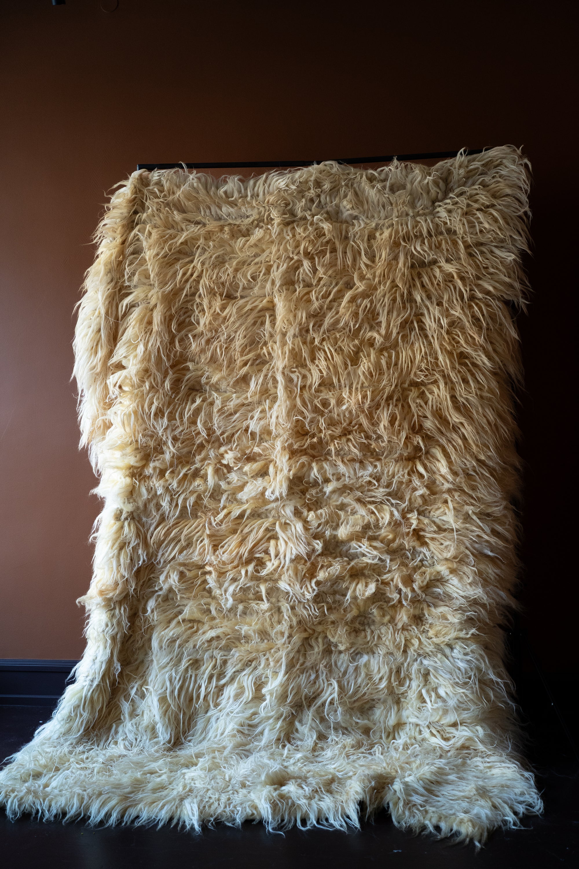 Marie Olsson Nylander Amber Rug hand-woven high-pile longhair wool Fuzzy Shepherd rug in cream beige hanging on a rail.

