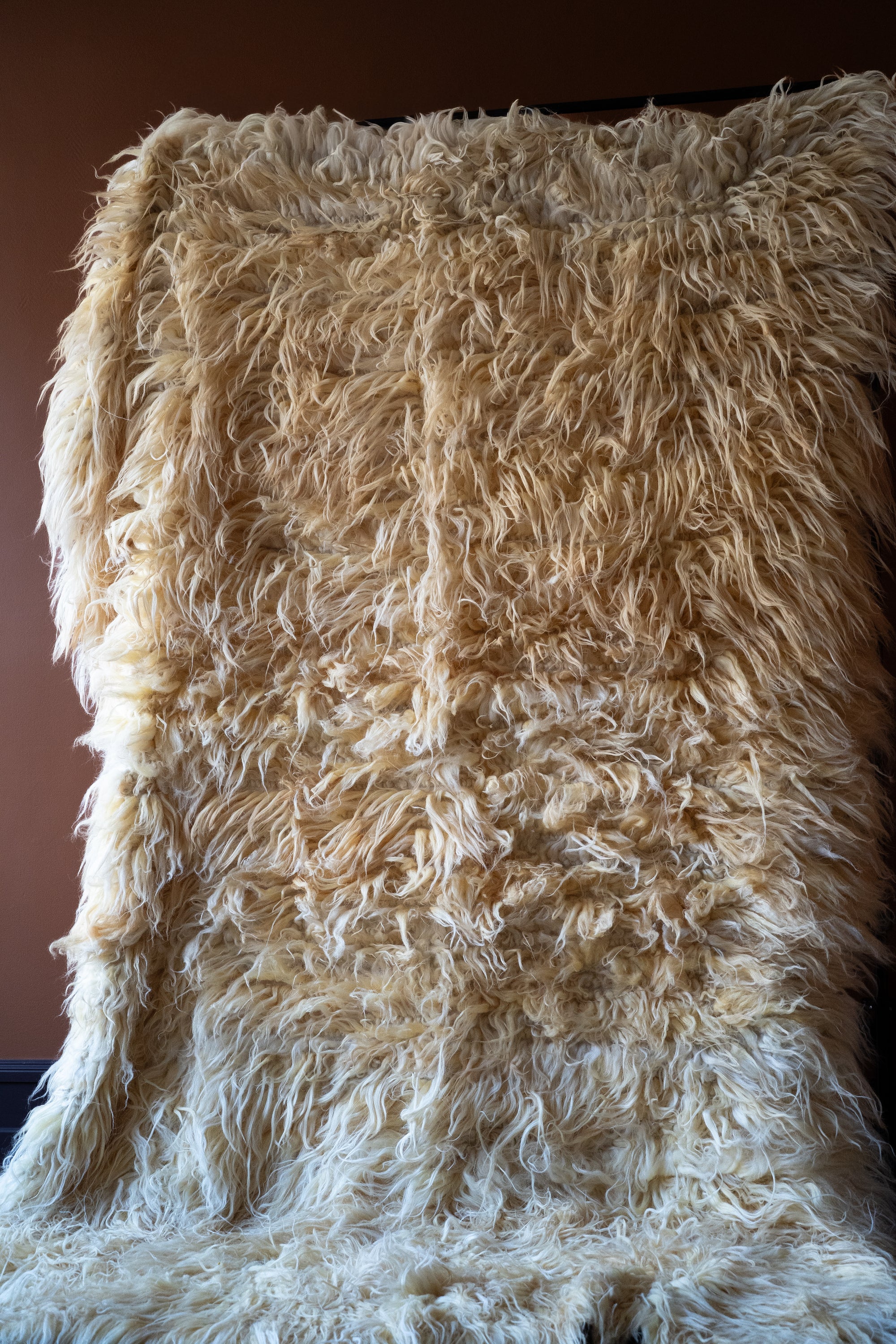 Marie Olsson Nylander Amber Rug hand-woven high-pile longhair wool Fuzzy Shepherd rug in cream beige hanging on a rail.
