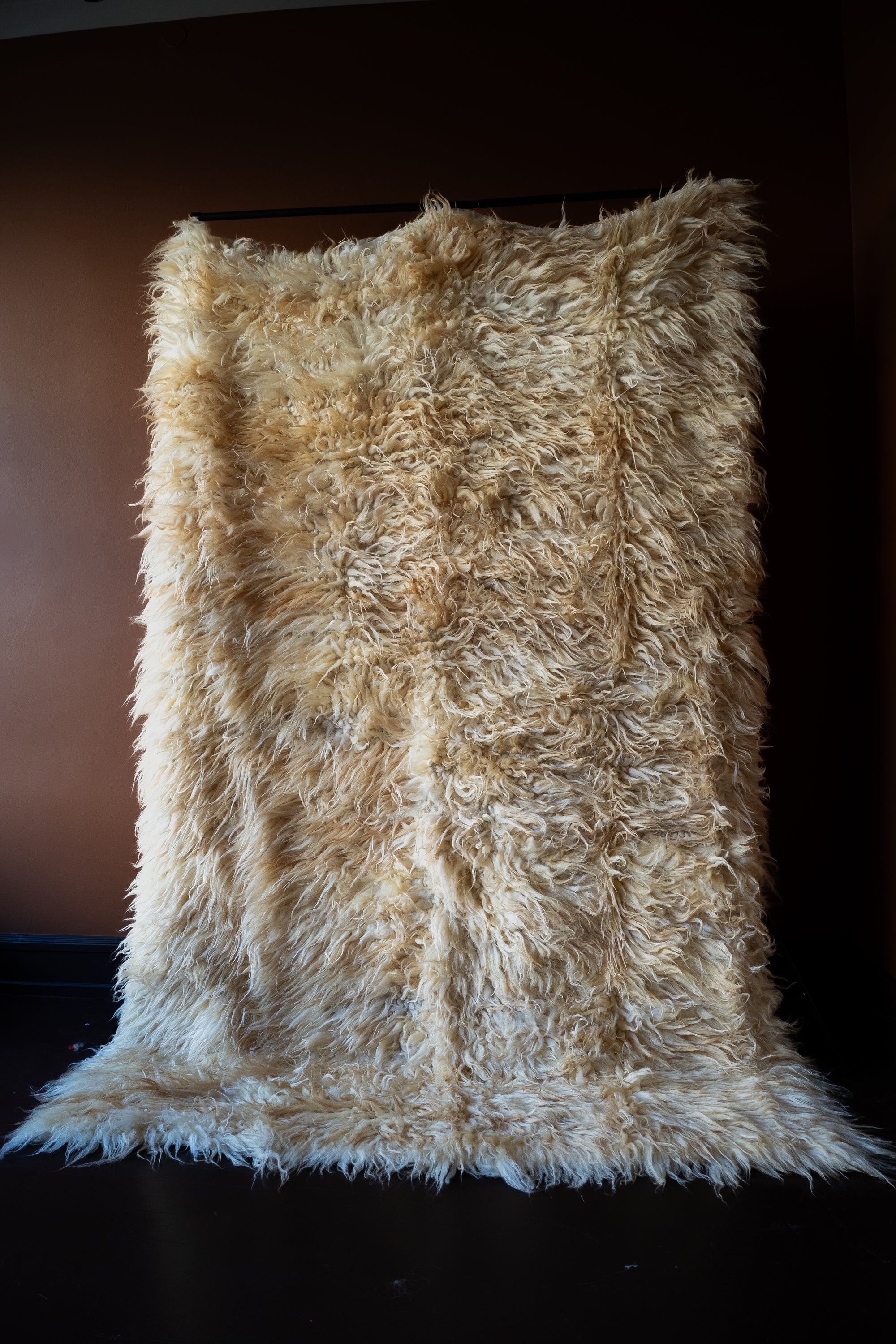Marie Olsson Nylander Amber Rug hand-woven high-pile longhair wool Fuzzy Shepherd rug in cream beige hanging on a rail.