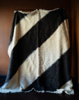 Marie Olsson Nylander hand-tufted Ukrainian wool blanket rug with wide diagonal black and cream graphic blockstripes resembling a traditional Lizhnyk throw.