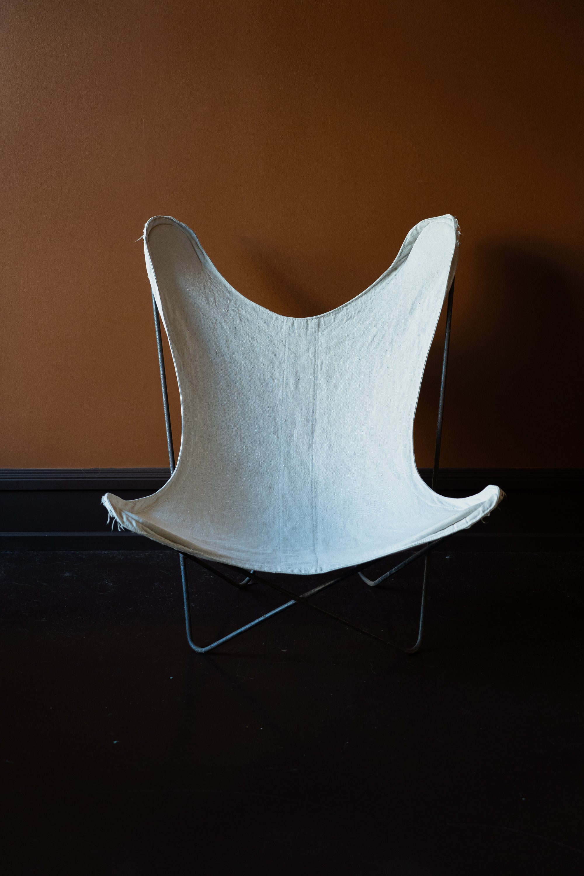 Authentic original 1960s Knoll BKF Butterfly Chair designed by Ferrari-Hardoy with an off-white French linen canvas cover against a brown wall.