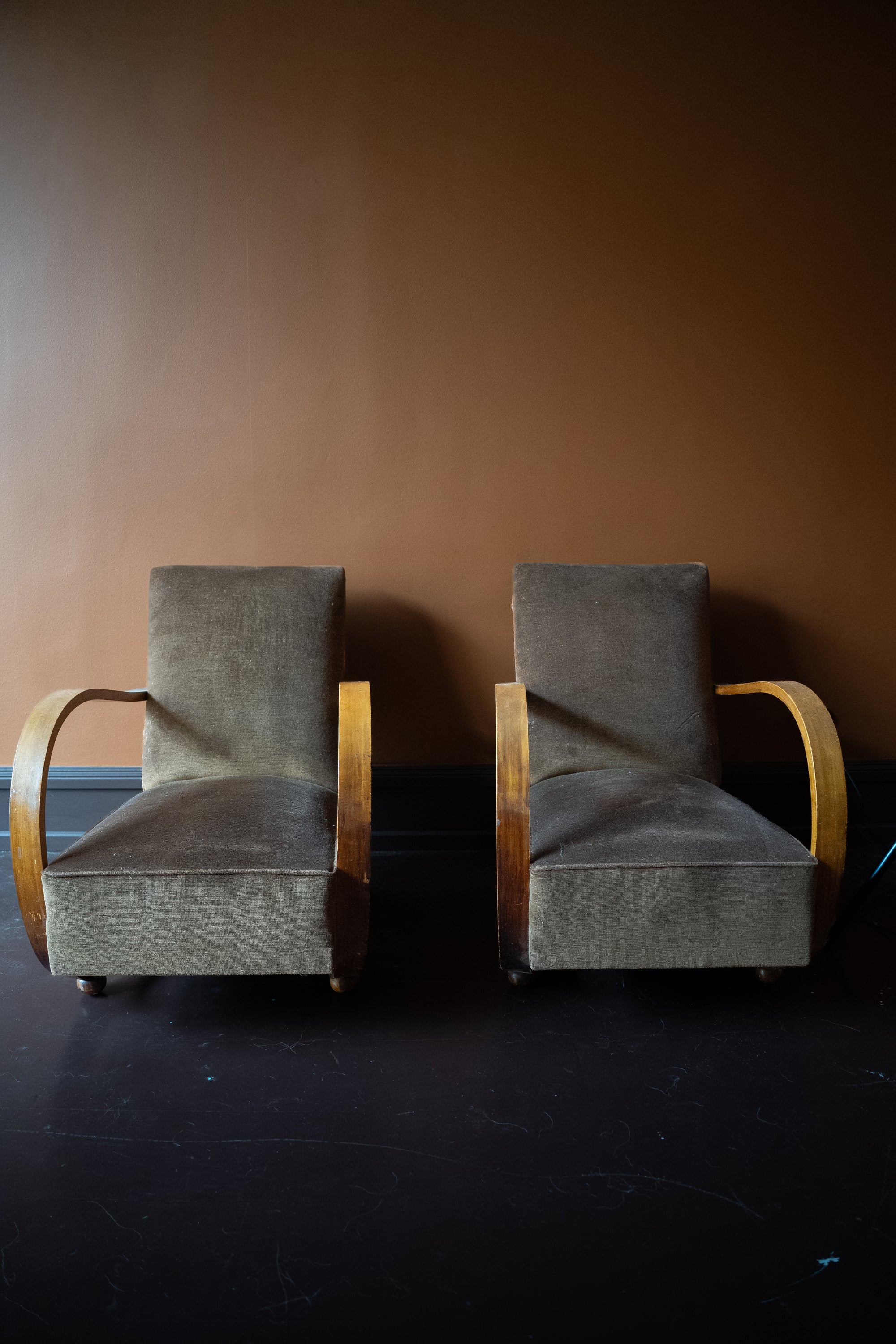 Pair of vintage French Art Deco armchairs from Avignon with sweeping bentwood armrests and olive bronze velvet upholstery against a brown wall.
