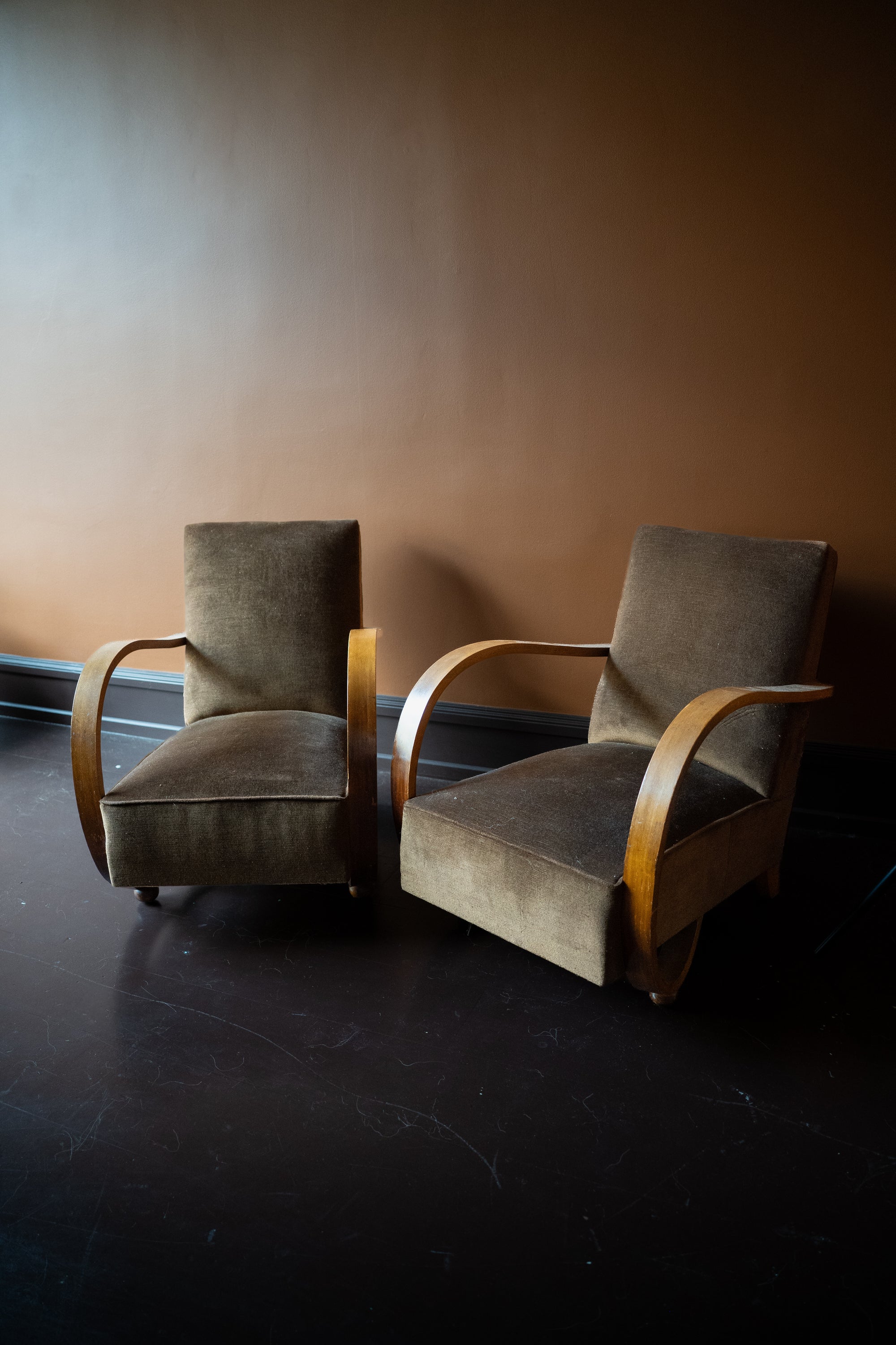 Pair of vintage French Art Deco armchairs from Avignon with sweeping bentwood armrests and olive bronze velvet upholstery against a brown wall.