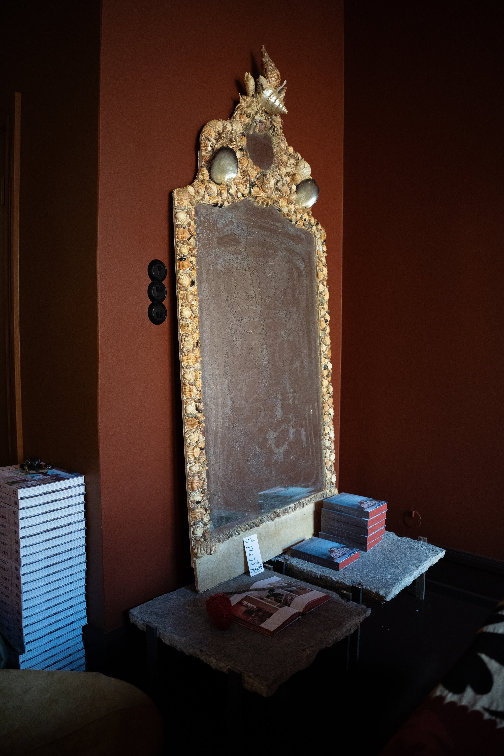 Huge 2-meter-tall vintage French grotto shell mirror handcrafted with natural sea shells standing on stone plinths against a terracotta wall.