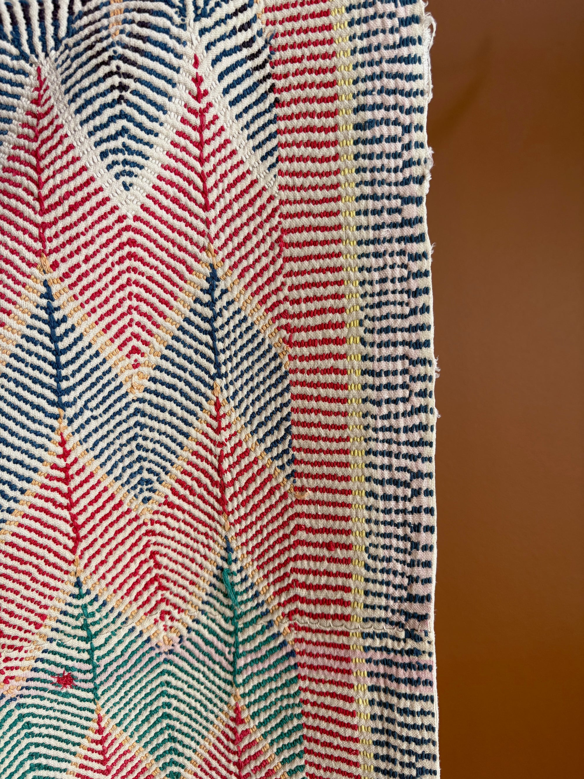 Semi-antique Jaipur Kantha quilt with a pink and mint green chevron zig-zag pattern hanging on a clothing rack against a terracotta wall.