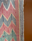 Semi-antique Jaipur Kantha quilt with a pink and mint green chevron zig-zag pattern hanging on a clothing rack against a terracotta wall.