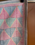 Semi-antique Indian quilt with a pink and mint green geometric triangle and diamond pattern hanging on a clothing rack against a terracotta wall.