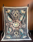 Semi-antique Indian quilt with a charcoal black base, large pink Suzani sun medallion, and turquoise paisley patterns hanging on a rack against a dark wall.