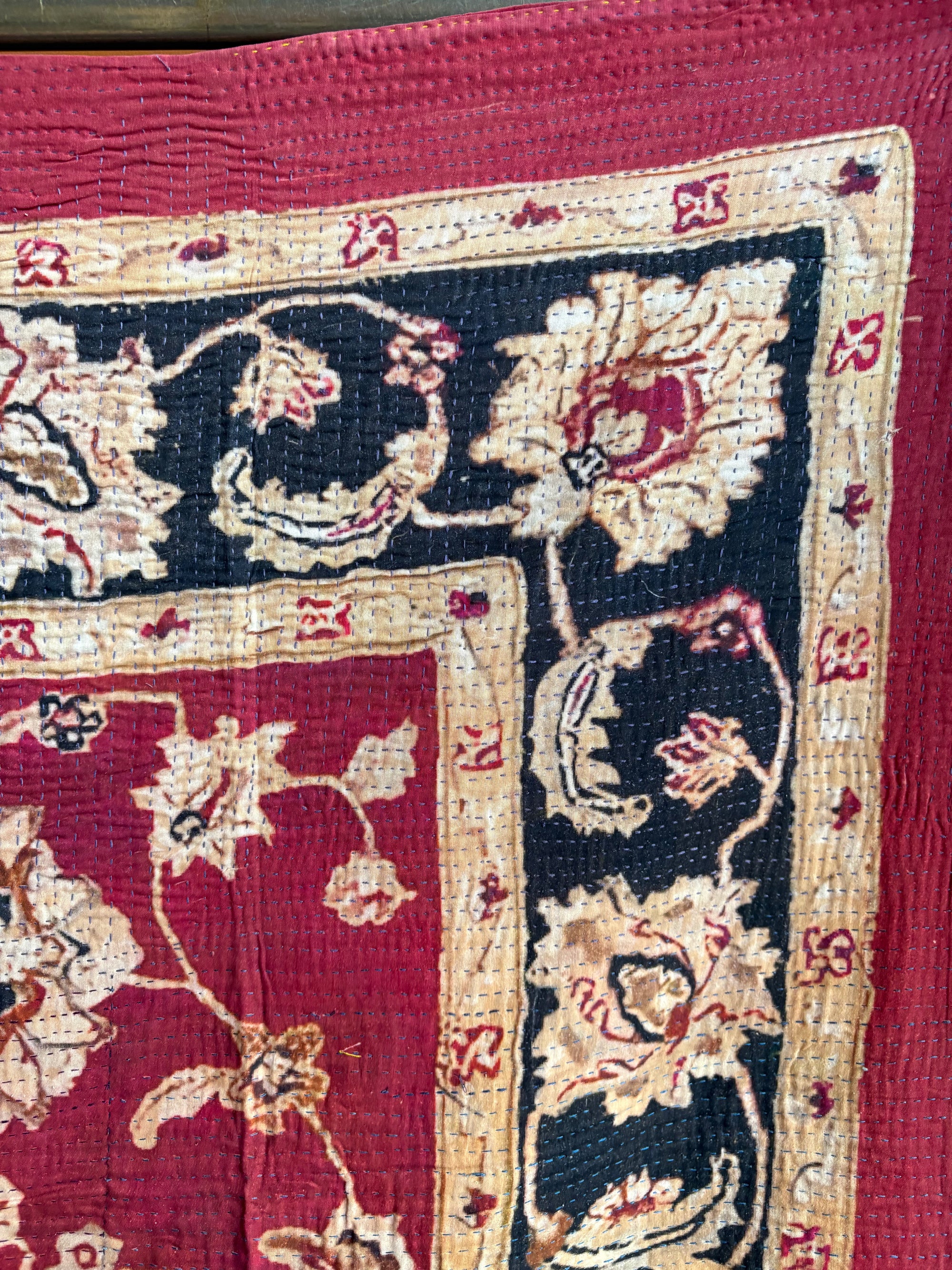 Semi-antique Indian quilt with a deep rust red base, ornate cream floral motifs, and a dark blue patterned border.
