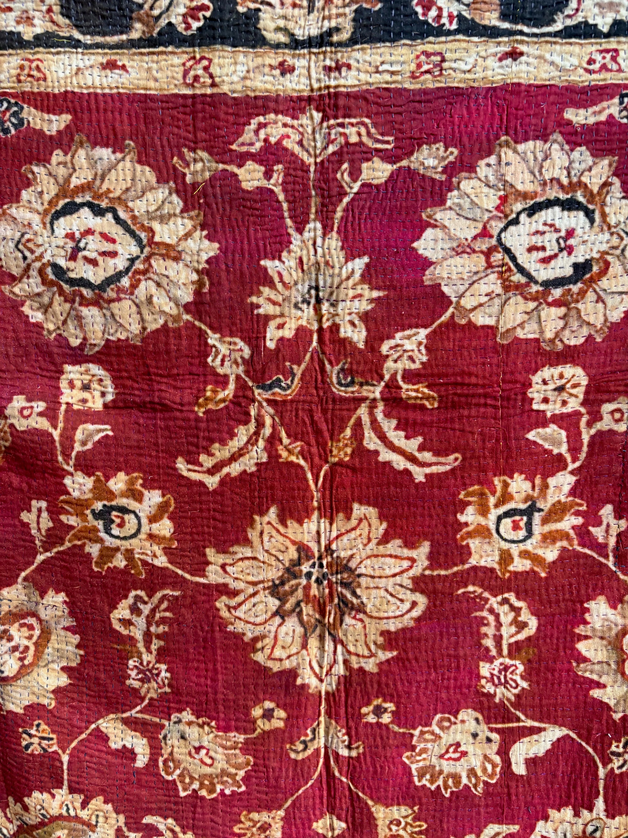 Semi-antique Indian quilt with a deep rust red base, ornate cream floral motifs, and a dark blue patterned border.